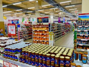 Wide view of a fully stocked supermarket aisle with jars and various products on shelves.